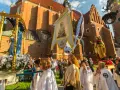 Prozession mit Marienstatue und Fahne vor einer Kirche. Menschen in weißen Gewändern, ein Festtag in Polen.