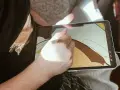 Osoba rysuje na ekranie iPad'a, używając rysika. To cyfrowy tablet graficzny, idealny do tworzenia sztuki.