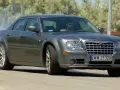 Szary Chrysler 300S z dymiącymi oponami, kierowca za kierownicą, na drodze.