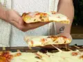 Due fette di pizza in teglia, con mozzarella filante e crosta dorata, vengono sollevate da mani.