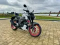 Biało-czarny Suzuki GSX S125 z czerwonymi felgami stoi na wybrukowanym placu nad jeziorem.