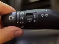Dłoń reguluje przełącznik świateł auto. Widoczne symbole oznaczają światła drogowe, mijania, postojowe i automatyczne.