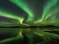 Grönt norrsken dansar över en frusen sjö i Finland. Stjärnor lyser på himlen och speglar sig i vattnet.