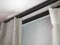 Ciemna szyna sufitowa z zasłonami w jasnych kolorach.