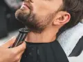Barbero perfilando barba con recortadora, creando diseños de barba modernos.
