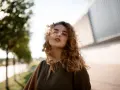 Kobieta z burzą kręconych włosów, wiatr rozwiewa jej kosmyki. Idealny przykład, jak utrwalić loki, by wyglądały naturalnie i pięknie.