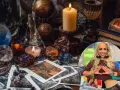 Mesa esotérica con cartas, cristales y velas. Una mujer sonríe haciendo un gesto con las manos, quizás buscando cómo atraer el amor.
