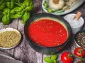 Schüssel mit leuchtend roter Pizza Sauce, umgeben von frischem Basilikum, Tomaten, Oregano, Salz und Pfeffer – wie in der Pizzeria.