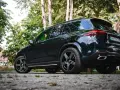 Ciemny Mercedes GLE 350 zaparkowany na kamienistej drodze, otoczony zielenią drzew.