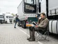 Kierowca odpoczywa przy ciężarówce, czytając książkę i pijąc kawę. Uważaj na mandat za skrócenie pauzy weekendowej!