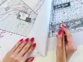 Dłoń z różowym lakierem na paznokciach trzymająca ołówek nad mapą projektową.