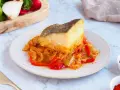 Un delicioso bacalao encebollado reposa sobre una cama de pimientos y cebolla.