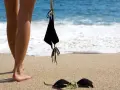 Nogi na piaszczystej plaży, obok czarny kostium kąpielowy. Fale obmywają brzeg. Idealne miejsce na naturystyczną plażę.