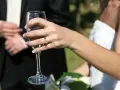 Dłoń panny młodej z pierścionkiem trzyma kieliszek szampana. W tle pan młody. 38 rocznica ślubu nazwa.