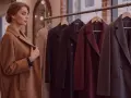 Donna osserva diversi tipi di cappotto in negozio: un cammello, un nero, un bordeaux e un grigio scuro.