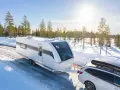 Vit husvagn dras av bil genom snöig skog. Den bästa husvagnen för äventyr nära Haparanda.