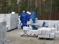 Budowa trwa! Pracownicy w niebieskich kombinezonach i białych kaskach układają bloczki ytong. Na paletach widać, że ytong 12 to spora ilość materiału budowlanego.