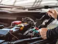 Mechanik sprawdza instalację elektryczną samochodu. Na zdjęciu widać multimetr i ręce trzymające sondy. Stojan z bezpiecznikami jest widoczny w tle.