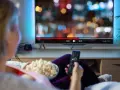 Persona relajada viendo una serie en francés en la televisión, con palomitas y mando a distancia.