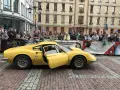Żółte Ferrari Dino z otwartymi drzwiami, kierowca w środku, tłum widzów za barierką.