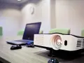 Rzutnik i laptop na stole, gotowe do prezentacji. Dowiedz się, jak podłączyć rzutnik do laptopa, by rozpocząć pokaz.