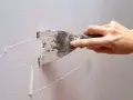 Mano usa una spatola per rimuovere la vecchia pittura, mostrando come grattare un muro per prepararlo.
