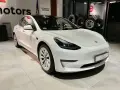 Biała Tesla Model 3 z napędem na cztery koła stoi w salonie samochodowym.