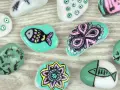 Ideas para pintar piedras de playa: peces, flores y diseños abstractos en tonos turquesa, blanco y rosa.