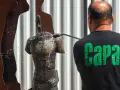 Hombre con camiseta negra "Capa" limpia una escultura de bronce con agua a presión.