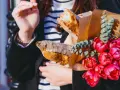 Kobieta trzyma świeżą bagietkę francuską, bukiet różowych tulipanów i gałązki eukaliptusa.
