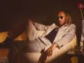 Ein Hip-Hop-Künstler in einem schicken Anzug entspannt sich auf einem Sofa, trägt Sonnenbrille und Schmuck.