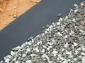 Gros plan sur un géotextile noir recouvert de gravier gris et blanc, à côté de sable. Idéal pour estimer le prix pose géotextile et gravier.