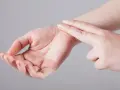 Dwa palce delikatnie naciskają na nadgarstek, pokazując, jak sprawdzić tętno.