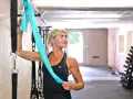 Kvinna med blont hår stretchar axlar med ett turkost träningsband i ett gym.