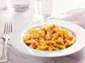 Piatto di pasta penne con speck e zafferano, guarnito con parmigiano e pepe nero.