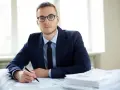 Mężczyzna w okularach i garniturze siedzi przy biurku z dokumentami. Zastanawia się, jak sprawdzić czy mam komornika.
