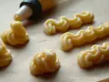 Kremowe eklery z czekoladą i profiteroles w trakcie przygotowania. Widać rękaw cukierniczy i wyciskane ciasto.