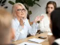 Kobieta w okularach, prezentująca kompetencje rady pedagogicznej, gestykuluje podczas spotkania.