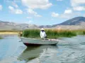 Donna con cappello di paglia rema su un lago, con montagne sullo sfondo. Mete agosto fuori Europa, un'immagine di pace.