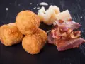Croquetas doradas y crujientes con trozos de bacon y queso sobre fondo oscuro.