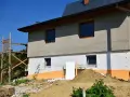 Budynek w trakcie ocieplania styropianem. Widoczne okna, rusztowanie i ziemia. Trzeba uważać na **mostek termiczny** przy oknach.