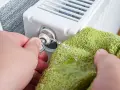 Odkręcanie odpowietrznika kluczykiem, by rozwiązać problem, dlaczego grzejnik jest zimny na dole. Woda kapie na zieloną ściereczkę.