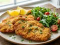Milanesa de pollo dorada y crujiente, servida con ensalada fresca de rúcula y tomates cherry, acompañada de gajos de limón.