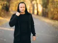 Mężczyzna w czarnej bluzie męskiej Guess z kapturem, stojący na ścieżce w jesiennym parku.