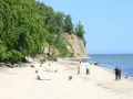 Słoneczny dzień na plaży przy klifie orłowskim. Ludzie spacerują, odpoczywają, a morze spokojnie faluje.