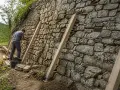 Un homme travaille à comment consolider un mur en pierre, utilisant des étais en bois pour soutenir la structure ancienne.