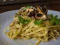 Pasta con champiñones, carne picada y queso rallado, decorada con hojas verdes.