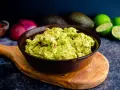 Miseczka guacamole z awokado, cebulą i limonką na drewnianej desce.