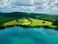 Acque turchesi del lago di Martignano lambiscono dolci colline verdi, con un casale isolato tra i campi.