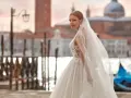 Sposa con abito da sogno e velo svolazzante a Venezia, con gondola blu sullo sfondo. Perfetta per un matrimonio da favola, anche con stivali sposa.